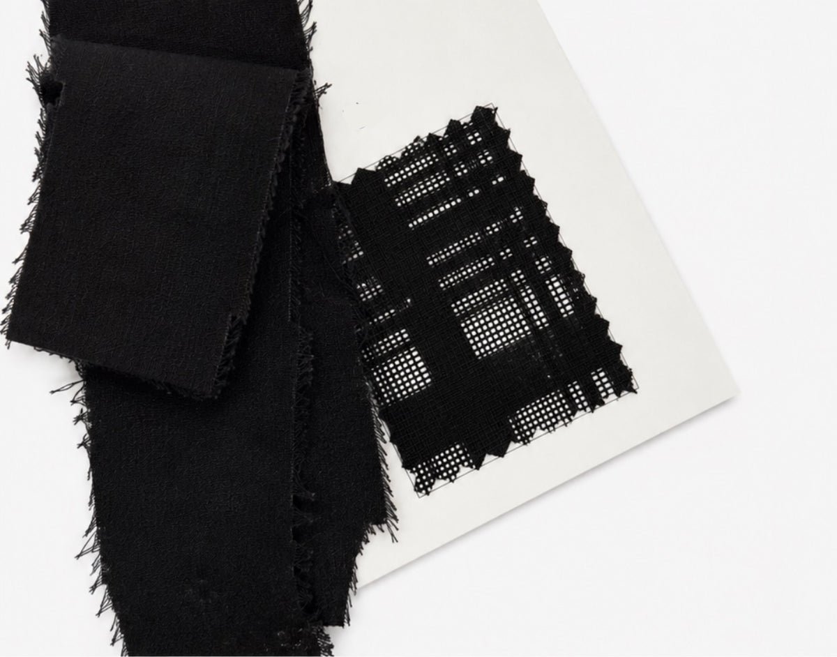 Black woven Karami-ori fabric swatches with frayed edges, including a solid black square and a black-and-white plaid-patterned square, displayed on a white card against a white background.